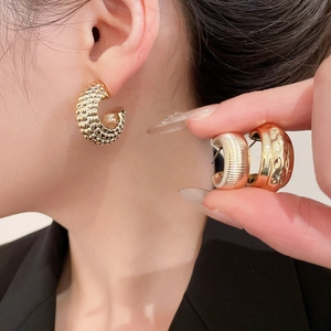 Detail view of gold C-shaped hoop earrings with hammered and textured metal finishes