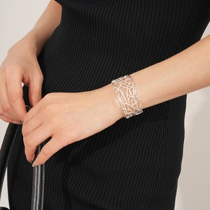 Gros plan d'un bracelet manchette évidé en maille argentée sur le poignet