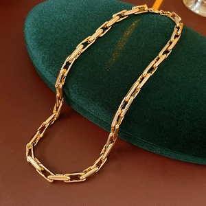 Detail of gold rectangular link chain necklace displayed on premium green velvet cushion