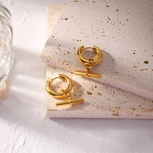 Detail of gold geometric T-bar charm earrings on elegant minimalist stone pedestals