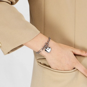 Silver heart pendant bracelet with OT clasp toggle closure worn on a wrist with khaki suit