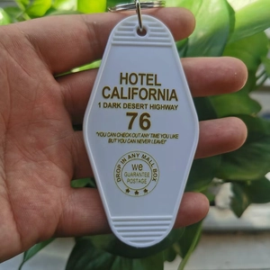 Close-up of white diamond-shaped vintage Hotel California 76 keychain with gold text