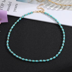 Handmade beaded necklace with turquoise cylinder stones and golden accents on a split background