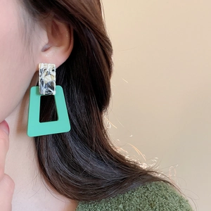 Detail of geometric acrylic marble earrings in mint green worn by a model in soft light