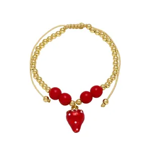 Detail of beaded gold bracelet featuring red strawberry pendant and adjustable cord