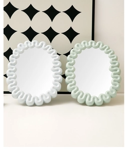 Detail of oval cream-style makeup mirrors with wavy frames in white and light green colors