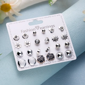 Macro shot of 12 pairs of silver earrings with flowers, stars and rhinestones on a white card