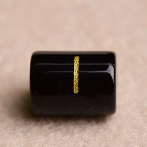 Close-up of black cylindrical bead with vertical gold stripe for DIY jewelry making