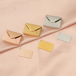 Polished metal envelope pendants and rectangular tags on pink silk fabric background