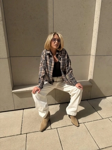 Outdoor shot of grey-brown plaid long-sleeve shirt paired with white trousers and suede boots