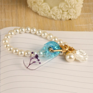 Macro detail of resin heart bookmark with purple dried flowers and gold pearl charm