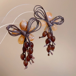 Macro shot of amber flower bead earrings with brown woven bow and deep red tassel fringe