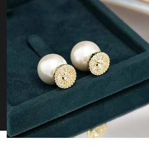 Detail of double-sided gold earrings with zircon starburst and large pearl on green velvet