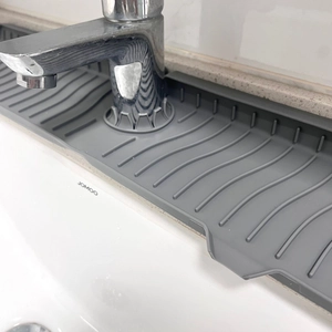 Close-up of grey silicone faucet mat showing drainage ridges on a white sink