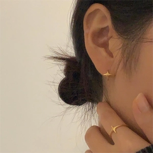 Close-up of a model wearing golden starburst stud earrings and a matching minimalist ring