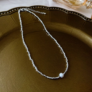 Close-up of silver beaded necklace with white pearl on a vintage gold luxury tray