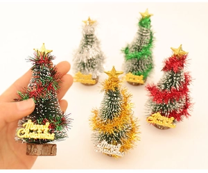 Mini artificial Christmas trees with wooden base and Merry Christmas sign in hand