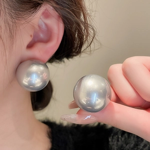 Close-up of a model wearing large silver spherical stud earrings with metallic finish
