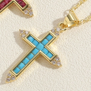 Macro shot of 14K gold plated cross pendant with turquoise and ruby gemstones