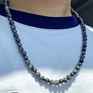 Close-up of beaded necklace with grey spotted and black polished stones on a model