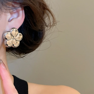 Polished silver flower stud earring worn by a model in a high-fashion close-up view