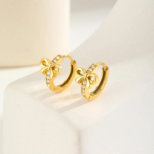 Elegant gold bow earrings with crystal inlay displayed on a minimalist geometric prop