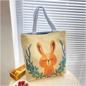 Detail of beige canvas tote bag with orange rabbit embroidery and floral wreath design