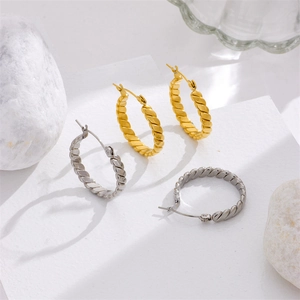 Twisted gold and silver titanium steel hoop earrings displayed on white pebbles
