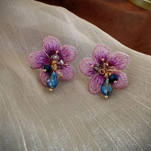 Détail de boucles d'oreilles fleurs en tissu violet avec perles de cristal et pendentifs