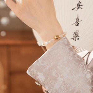 Detailed view of white crystal bead bracelet with engraved golden sphere on the wrist