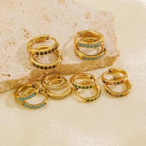 Polished gold huggie hoop earrings with colorful zircon inlay on textured stone background