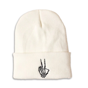 Close-up of white knitted beanie with black skull hand victory gesture embroidery