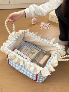 Detail of blue plaid fabric storage basket with white ruffles and pearl handle