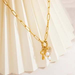 Gold paperclip necklace with heart diamond pendant, key charm and pearls on white background