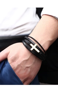 Dettaglio del bracciale multistrato in pelle nera intrecciata con croce d'oro