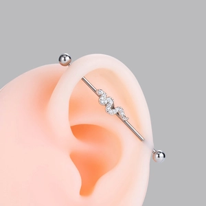 Macro detail of silver industrial barbell with zircon-encrusted snake on model ear