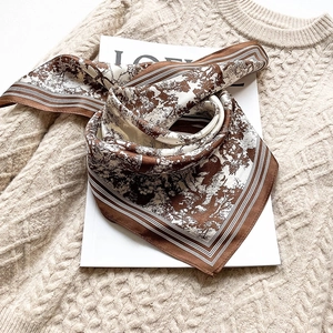 Elegant silk square scarf with brown tree prints layered on a beige knit sweater