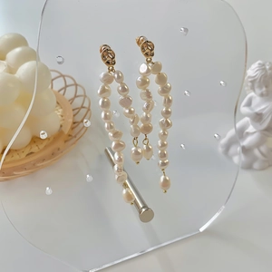 Close-up of long baroque freshwater pearl tassel earrings on a luxury display stand