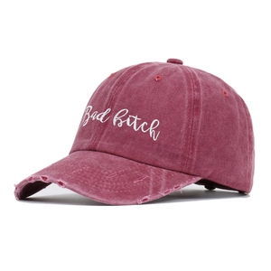 Detail of distressed burgundy baseball cap featuring white Bad Bitch embroidery and torn brim