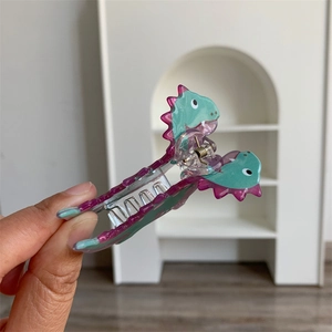 Detailed close-up of a cute green acrylic dinosaur hair claw clip with pink fin details