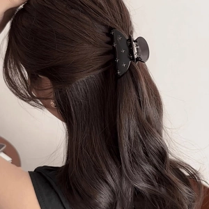 Pince à cheveux noire semi-circulaire avec strass portée sur longs cheveux bouclés