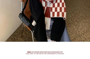 Close-up of red and white checkered knit scarf paired with black woven leather handbag