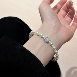 Close-up of pearl necklace with square green chalcedony pendant on a model's wrist