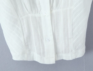 Detail of white jacquard fabric with vertical pleats and buttons on polo top