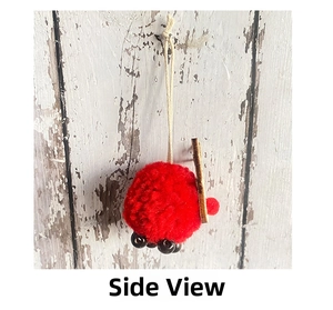 Side view of red plush pom-pom reindeer ornament with wooden part on white wood background