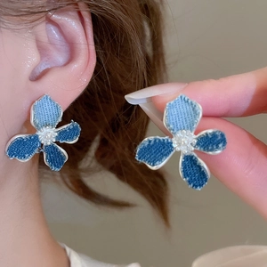 Detail of blue denim floral C-shaped earrings with faux pearl centers and silver trim