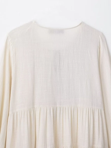 Detailed view of embroidery stitching and linen fabric texture on an off-white dress