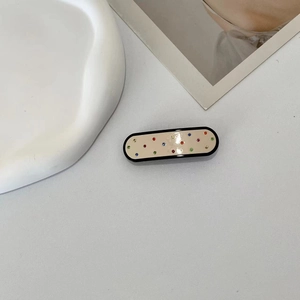 Close-up of cream acetate hair claw clip with colorful rhinestones and black border