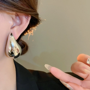 Close-up of a large silver water drop metal earring with mirror-polished finish on a model