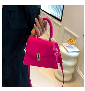 Detail of rose red trapezoid handbag with gold hardware and removable shoulder strap